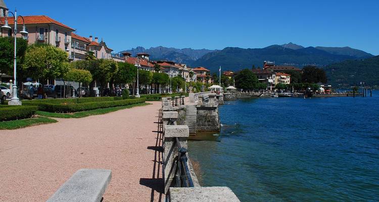 Paseo junto al lago con setos y montañas al otro lado del azul Lago Mayor en Baveno