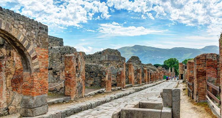 Ancient stone street and brick columns of the archaeological site of Pompeii with visitors exploring the ruins.