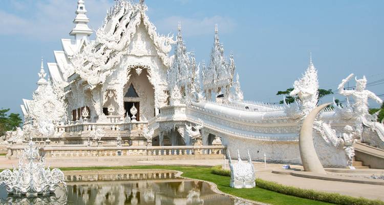 De oogverblindend witte gevel van Wat Rong Khun weerspiegelt zich op een heldere dag in een vijver.