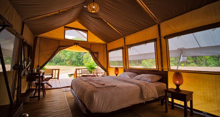 Ruime luxe safaritent met een kingsize bed die uitkomt op een houten terras en uitzicht op de jungle.