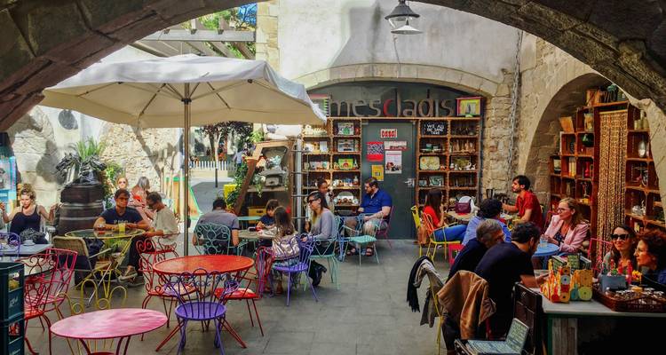 Café colorido en el patio lleno de gente disfrutando de comida y bebidas.