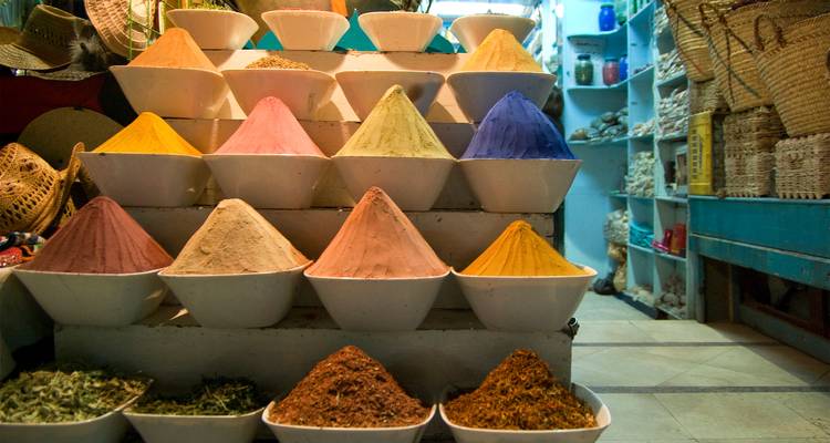 Hileras ordenadas de cuencos blancos llenos de especias en polvo de colores brillantes en exhibición dentro de un mercado