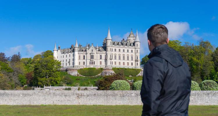 Ein Besucher bewundert die majestätischen weißen Türme von Dunrobin Castle, die sich über gepflegten Gärten erheben.
