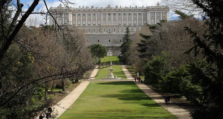 Vista enmarcada por árboles del Palacio Real de Madrid con vistas a los cuidados Jardines de Sabatini.