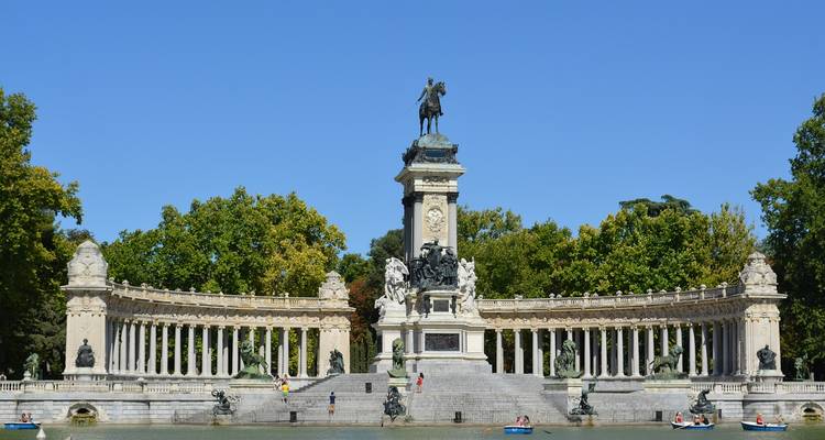Gran monumento con columnata curva y estatua ecuestre reflejada en un estanque en un día soleado y brillante