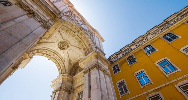 Vista hacia arriba de un gran arco de triunfo y un edificio histórico amarillo contra un cielo despejado