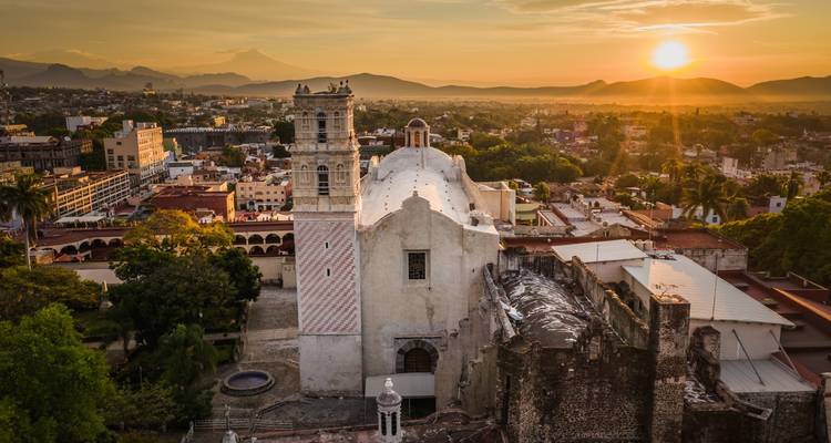 Vista de una iglesia al atardecer con montañas al fondo.