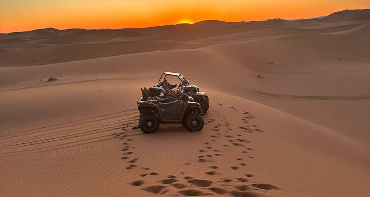 ATVs on sand dunes at sunset with tracks visible.