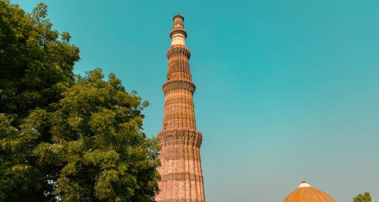 Qutub Minar mit einem klaren blauen Himmel und Bäumen.