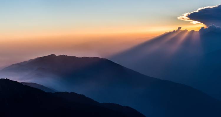 Sonnenstrahlen durchbrechen Wolken über einer nebligen Bergkette.