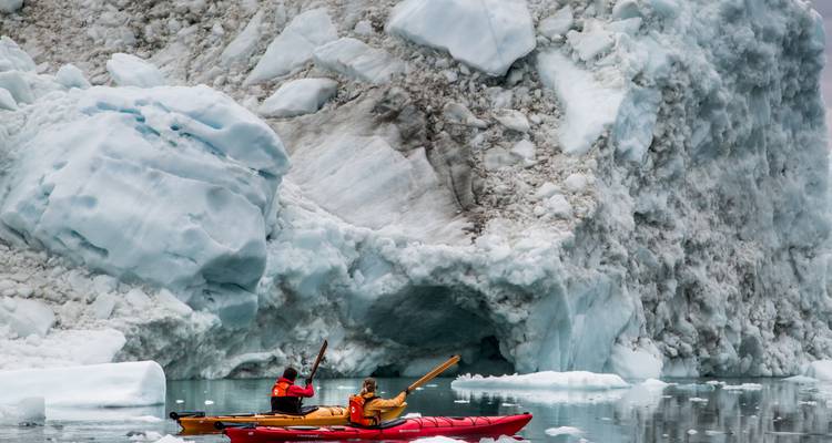 Kajakfahrer, die in der Nähe eines großen Eisbergs navigieren.