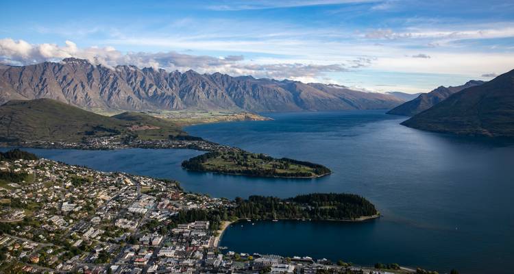 Vista aérea amplia de la península de Queenstown, lago tranquilo y cadena alpina dentada.