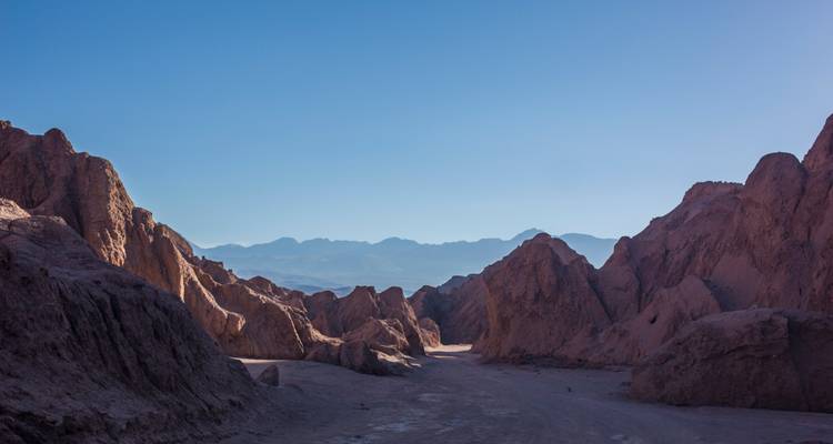 Les formations rocheuses ocre et accidentées encadrent une chaîne de montagnes andine lointaine sous un ciel bleu dégagé dans le désert d'Atacama au Chili.