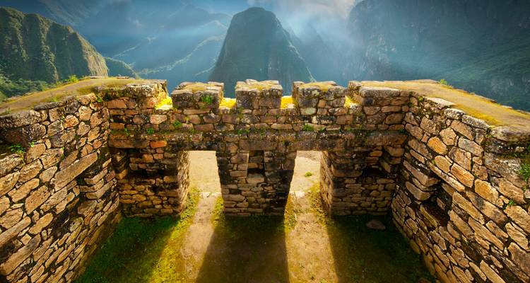 Ruinas antiguas con un telón de fondo montañoso, bañadas por la luz del sol.
