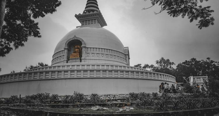 Stupa mit Statuen und Besuchern in einem Gartenbereich.