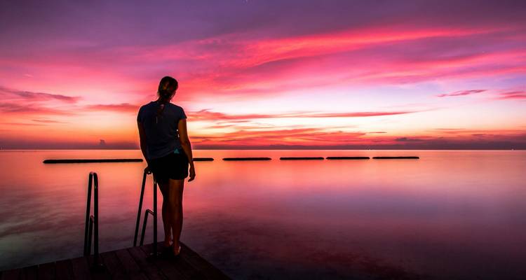 Silhouette einer Person, die einen lebendigen Sonnenuntergang über dem Ozean beobachtet.