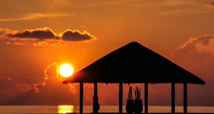 Silhouette einer strohgedeckten Hütte während eines lebendigen Sonnenaufgangs.