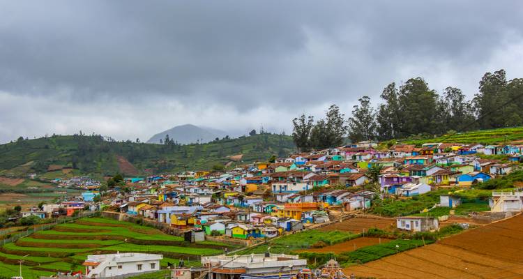 A patchwork town of colourful houses sprawls across green terraced hills beneath brooding clouds.