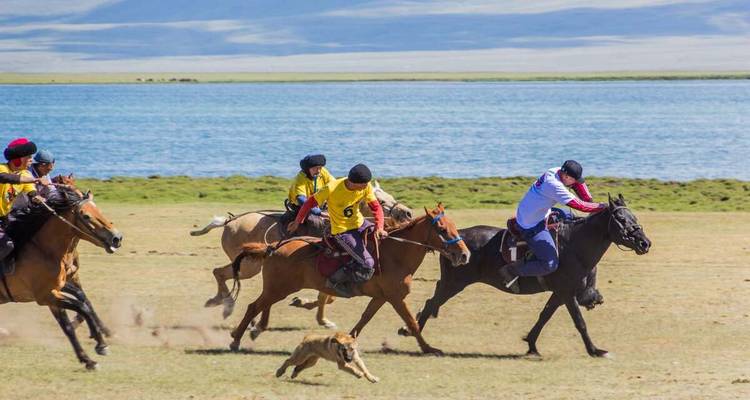 Horse riders in a race near a lake, with mountains in the background.