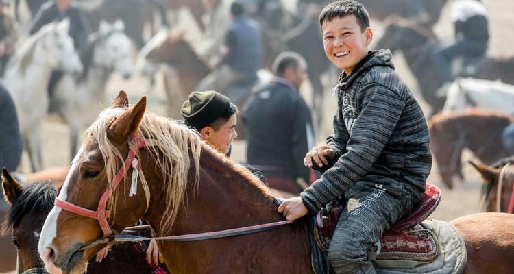 A smiling person riding a horse with a crowd in the background.