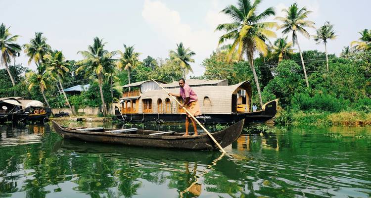 A man paddling a traditional canoe in a lush green waterway with houseboats.