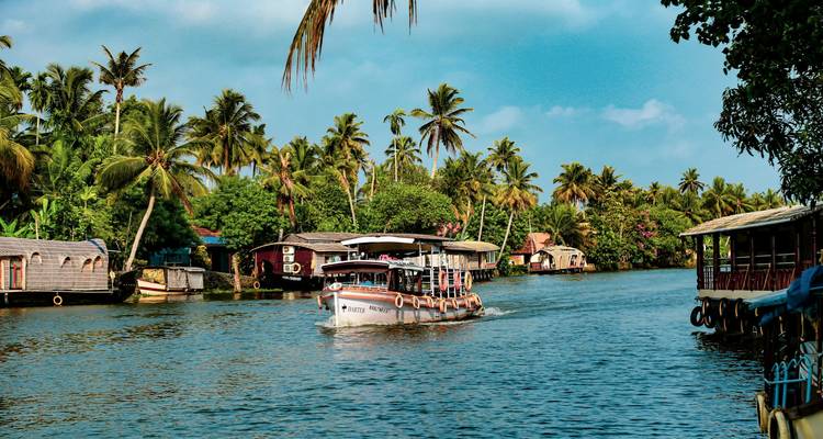 A boat on a scenic river surrounded by palm trees and traditional houses.