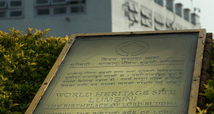 Tafel, die eine Welterbestätte kennzeichnet, mit einem Monument im Hintergrund.