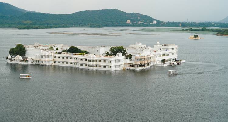 Iconic white Lake Palace appears to float on tranquil waters amid surrounding hills.