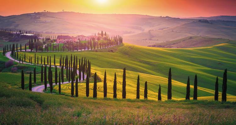 Hermoso paisaje toscano con una carretera serpenteante y cipreses al atardecer.