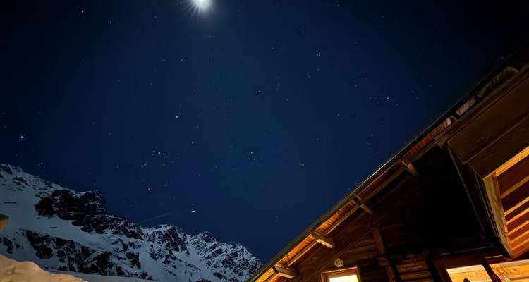 Une vue de nuit étoilée avec une cabane en bois et des montagnes enneigées.