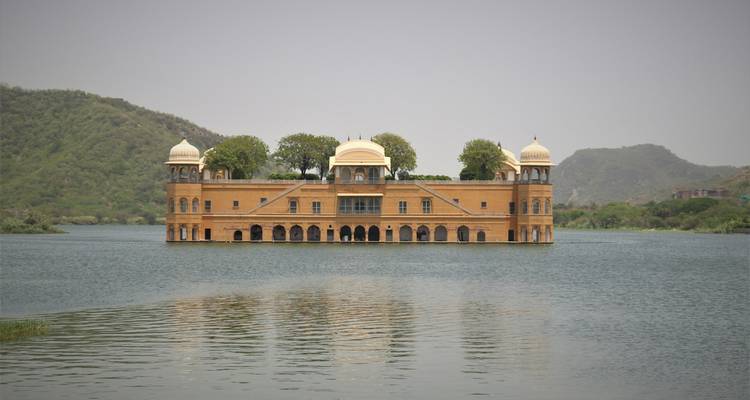 The sandstone Jal Mahal palace sitting mid-lake with hazy green hills in the background.