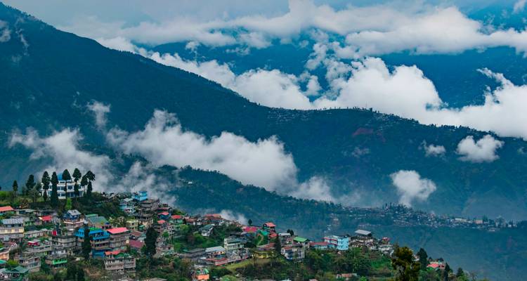 Une vallée de montagne brumeuse parsemée de maisons colorées sur les flancs de collines et de nuages qui s'évanouissent après la pluie.