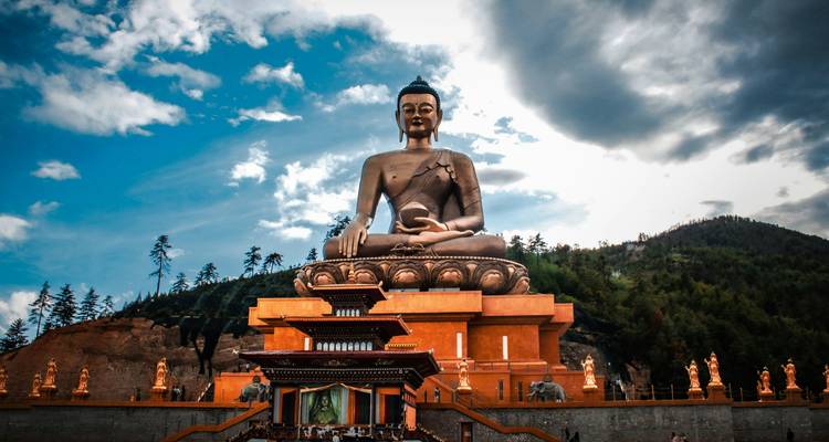 La gigantesque statue du Bouddha doré Dordenma s'élève au-dessus d'une cour de temple en étages sur un ciel dramatique.