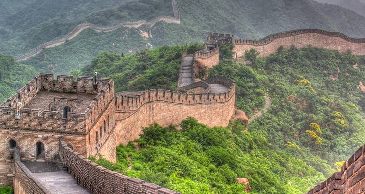 Die Chinesische Mauer an einem nebligen Tag, umgeben von üppigem Grün.