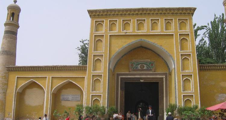 Yellow-tiled entrance of a grand mosque with people gathered outside and a tall minaret