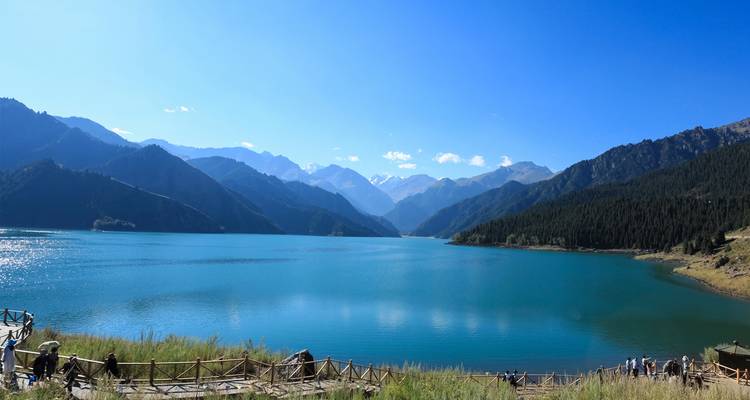 A serene alpine lake of deep blue water reflects rugged snow-capped mountain peaks beneath a crystal sky.