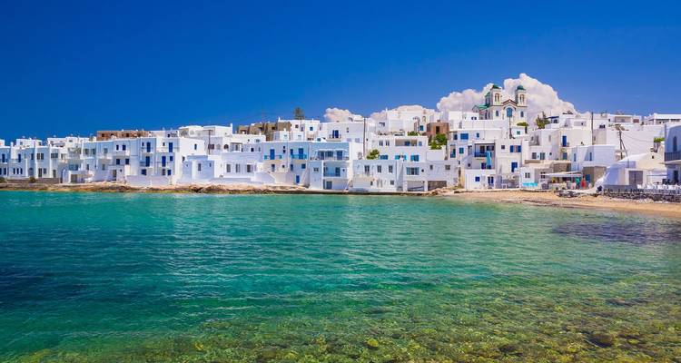 Village côtier aux maisons cubiques blanches donnant sur une baie aux eaux cristallines sous un ciel bleu profond.