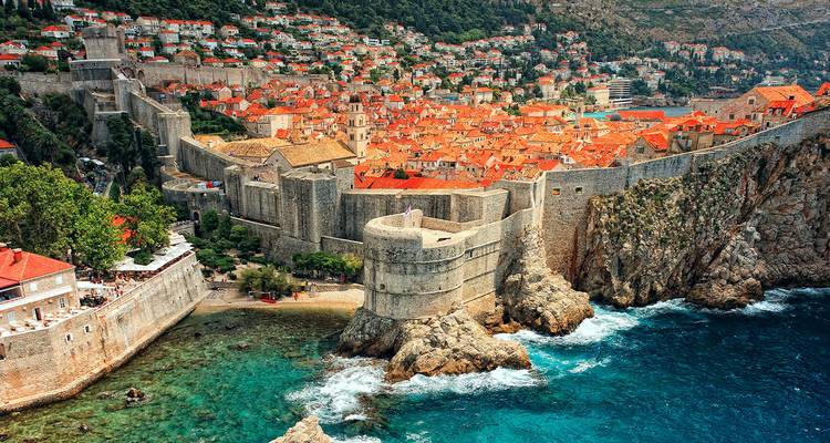 Dramatische luchtopname van Dubrovniks enorme stenen muren die op rotsachtige kliffen boven het türkooizen Adriatische water uitsteken