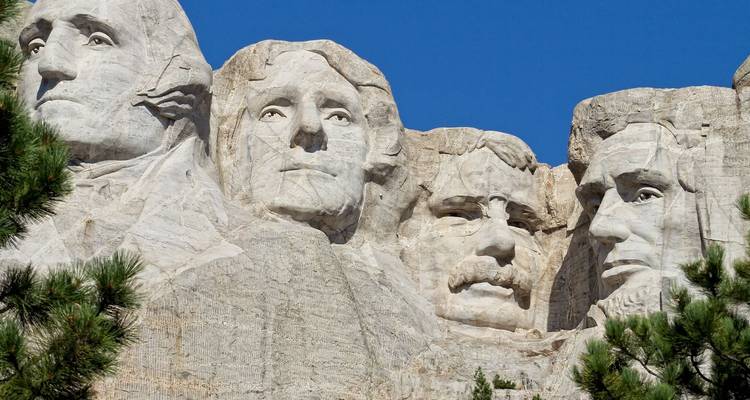 Les visages de granit de quatre présidents américains regardent depuis le Mont Rushmore sur un ciel bleu profond.