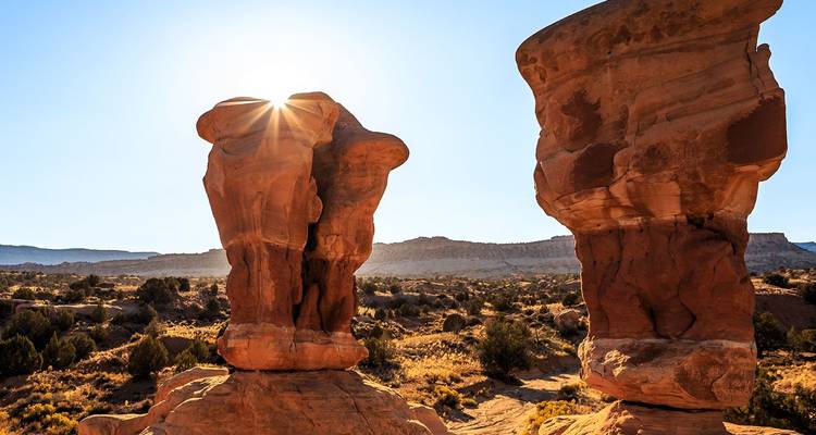 El brillo del sol asoma entre dos formaciones rocosas únicas de arenisca en el paisaje desértico de Utah.