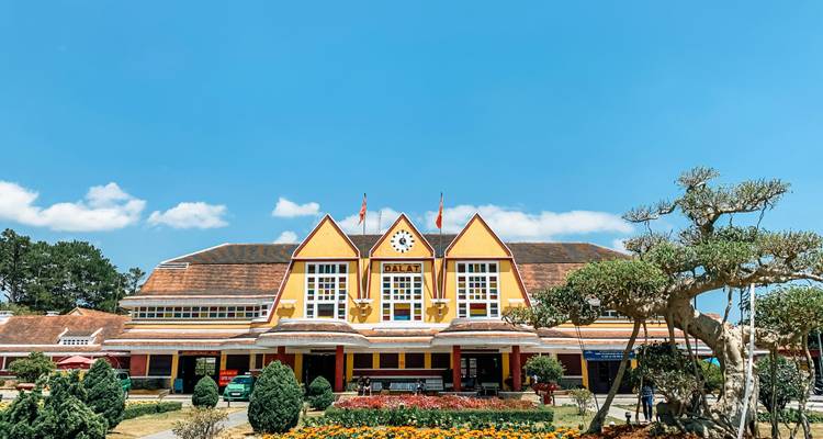 Bright yellow French-colonial style railway station building set against a vivid blue sky in Dalat.