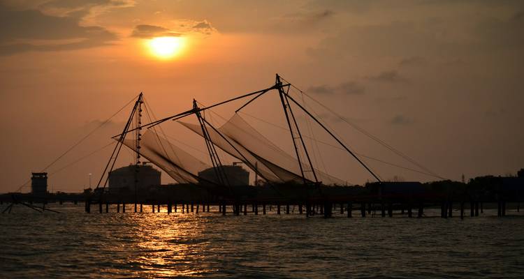Des filets de pêche chinois traditionnels se découpant en silhouette contre le soleil couchant.