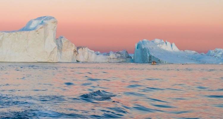 Lumière douce du coucher de soleil rose pâle sur les icebergs à la dérive et la mer arctique aux ondulations scintillantes.