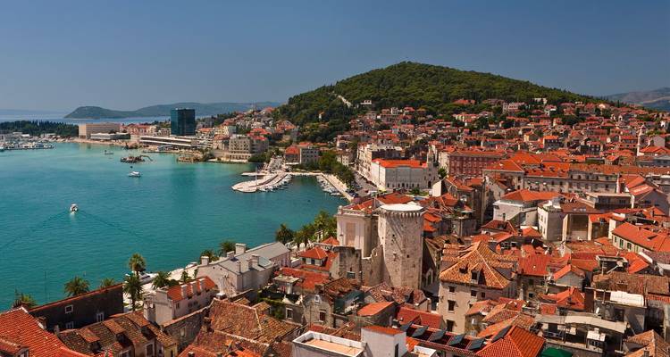 Vista panorámica del casco antiguo de Split con sus tejados rojos y el puerto turquesa, todo ello con un telón de fondo de colinas verdes.