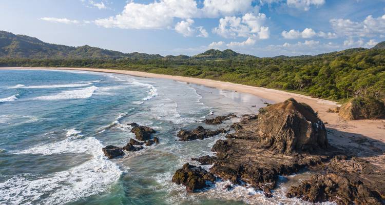 Felsige Küste mit Wellen und grünen Hügeln.