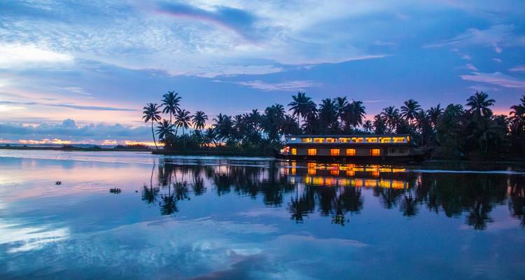 Ein Hausboot mit beleuchteten Fenstern auf einer ruhigen Wasserstraße in der Abenddämmerung.
