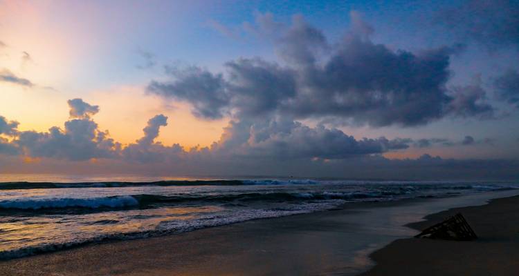 Ein ruhiger Strand bei Sonnenuntergang mit Wellen, die sanft an Land spülen.