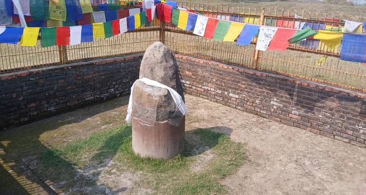 Ein stehender Stein, der in ein Tuch gehüllt ist mit bunten Gebetsfahnen.