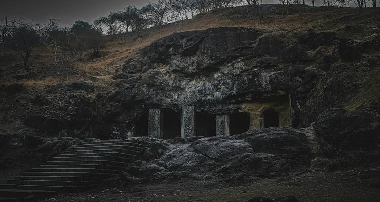 Cave entrances carved into a rocky hillside in a dark setting.