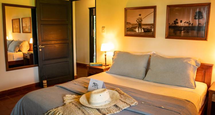 Gezellige slaapkamer met een bed, hoed, en warme verlichting, vintage kunstwerken aan de muren.